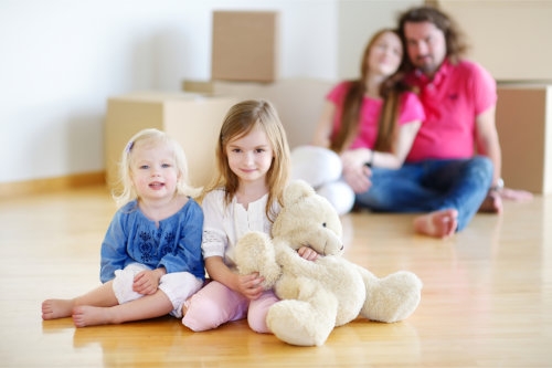 two little siblings sitting on the floor together with their parents behind them